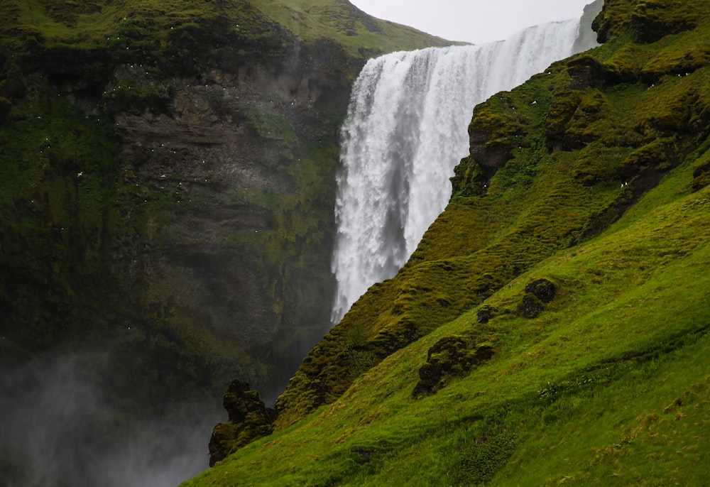 green grass-covered mountain beside waterfalls