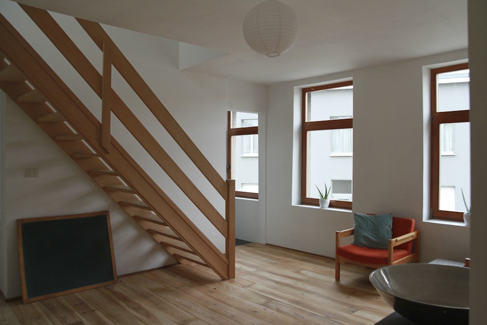 Brauner gepolsterter Sessel mit Holzrahmen und rotem Stoff in der Nähe von Treppe und Fenster während des Tages