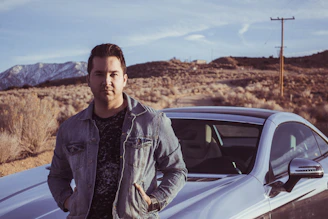 A confident traveler holding car keys standing next to a white SUV with forest hills in the background.