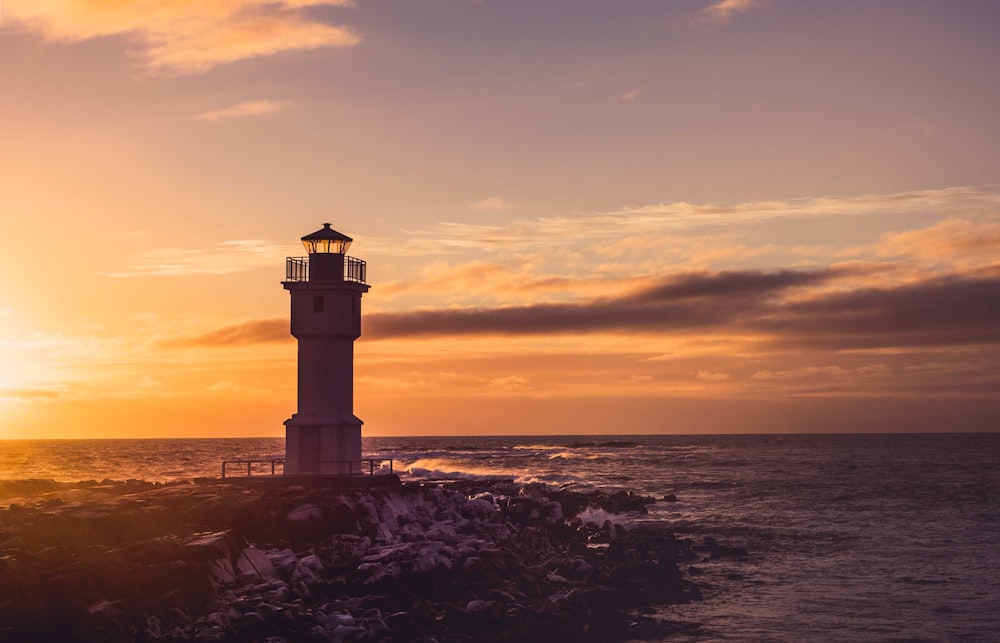 Torre do farol branco sob céu nublado amarelo e branco ao pôr do sol