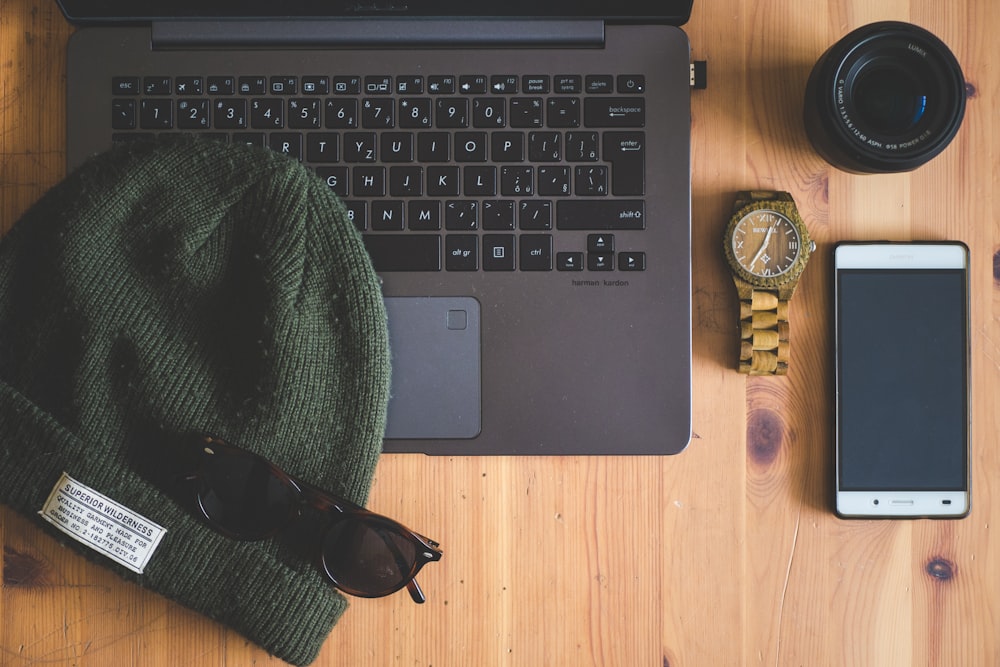 green knit cap on laptop near watch, smartphone, and camera lens