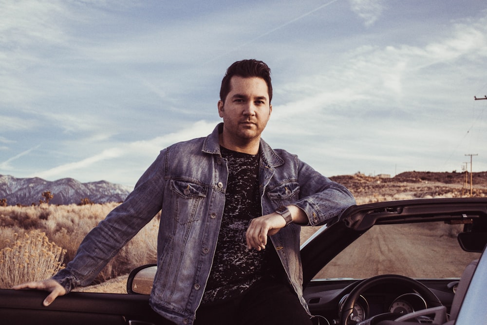 closeup photo of man wearing gray denim jacket leaning on car