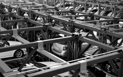 A complex structure of metal beams creates multiple levels for parking, filled with various cars. The intricate framework appears industrial and systematic, efficiently utilizing vertical space.