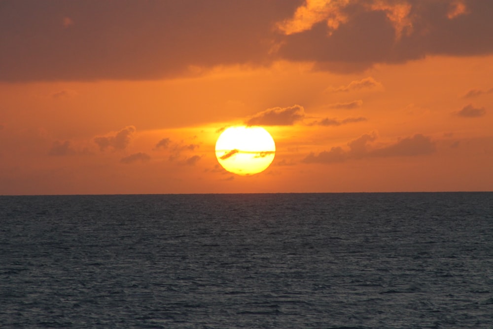 the sun is setting over the ocean on a cloudy day