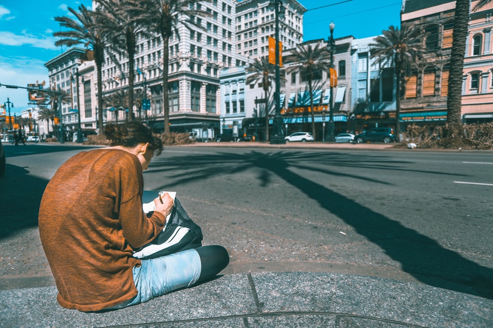 man sitting on road infront of brown concrete building under blue sky during daytime