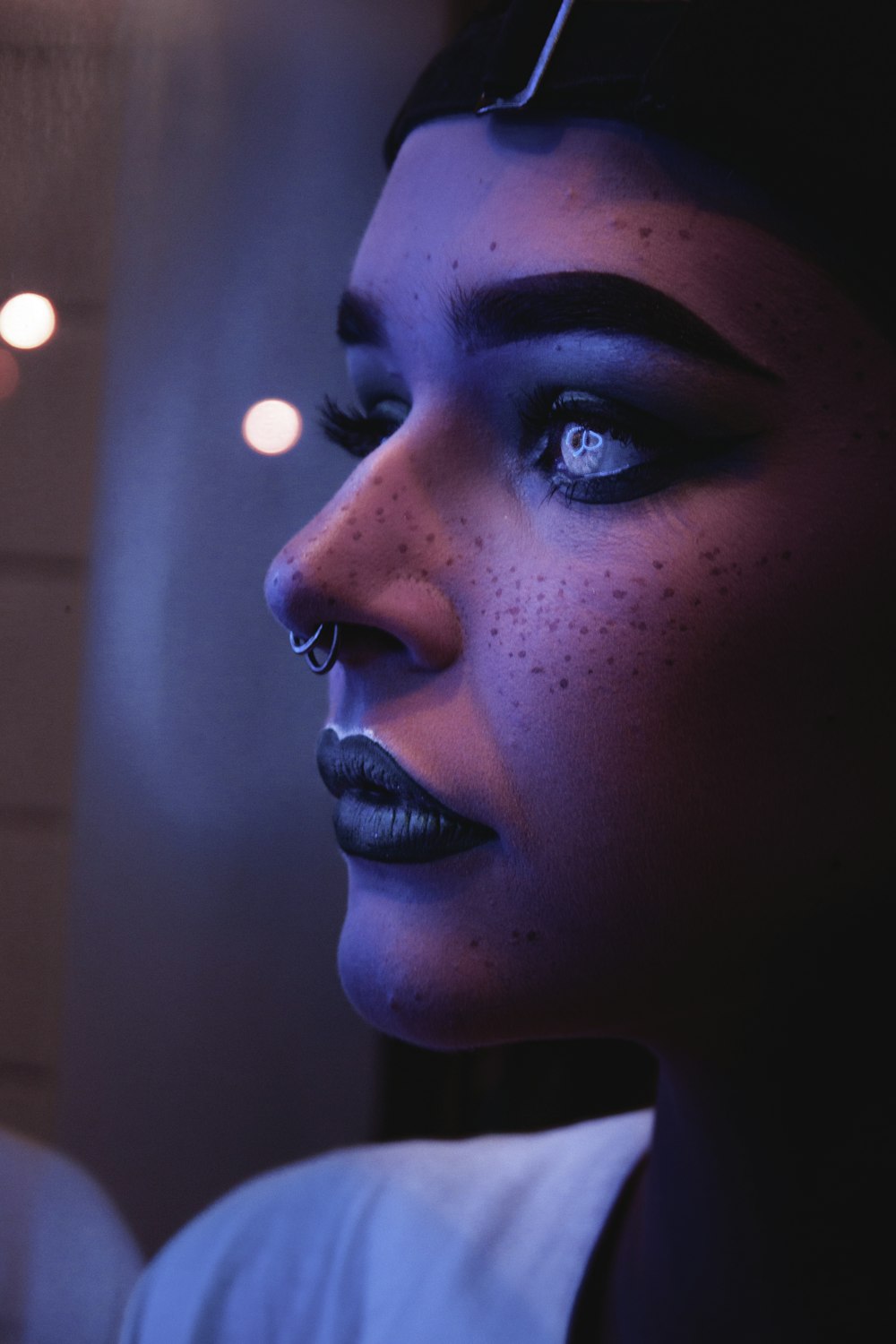 Foto einer Frau mit schwarzem Lippenstift und Nasenpiercings, aufgenommen in einem Raum mit gedämpftem Licht