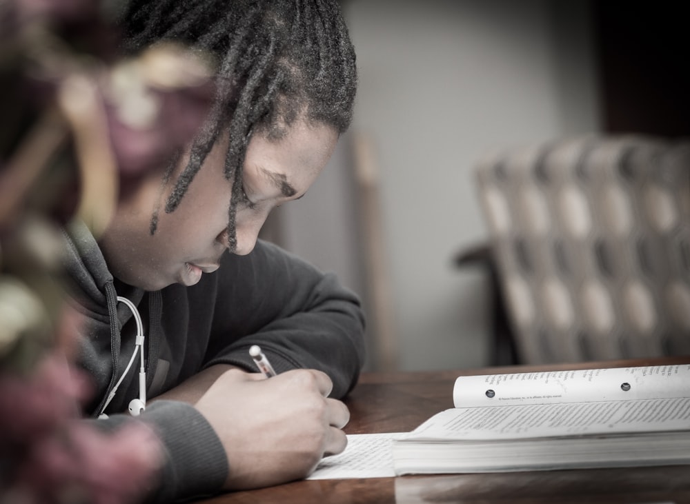 man writing on paper near book on table