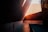 Strong angular architecture with dramatic lighting and deep shadows dominate the scene. The walls and surfaces are smooth, with a warm palette of browns and oranges. Geometric shapes create a play of light and shadow, casting sharp lines across the floor and walls.