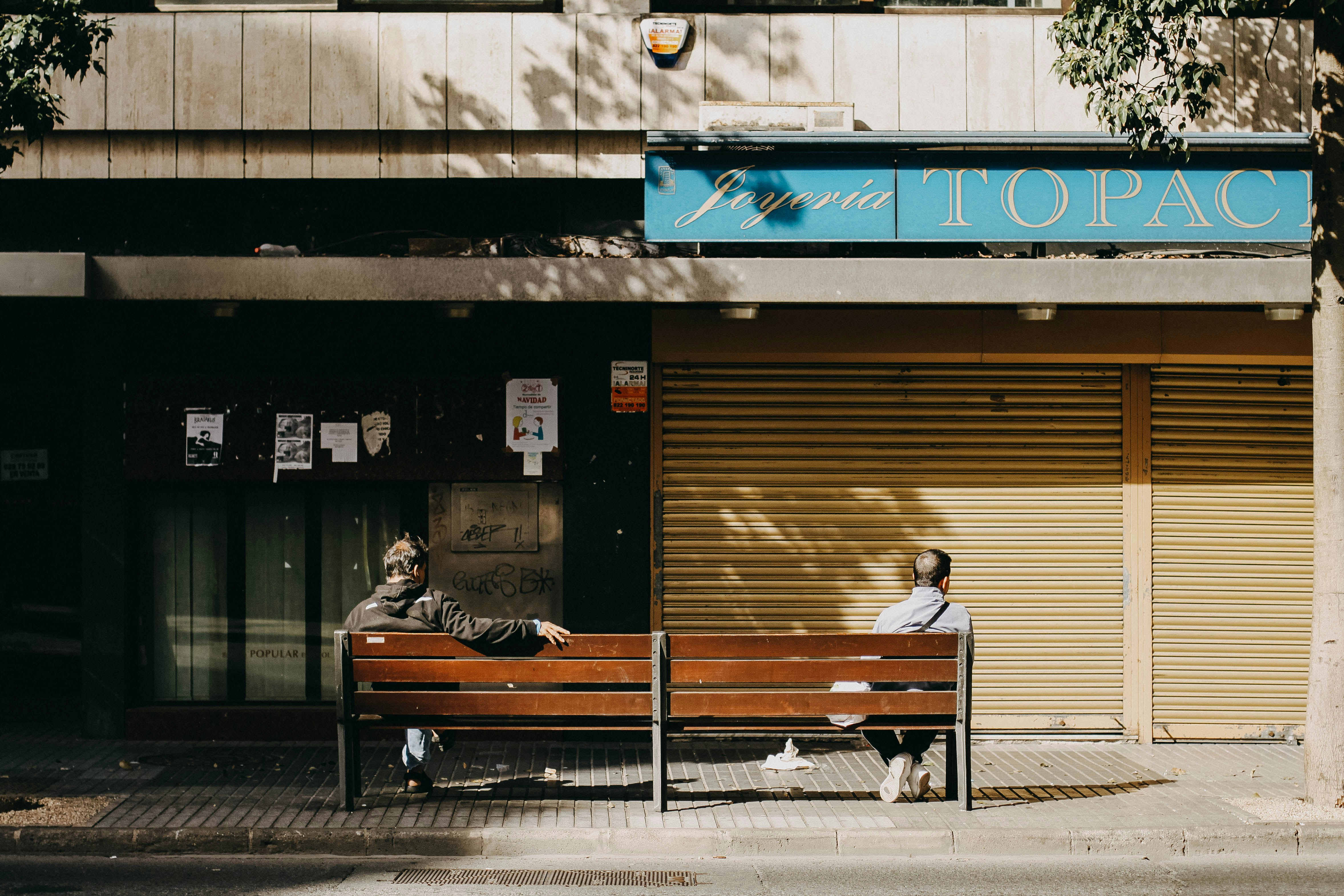 two persons sitting on bench near concrete buildings during daytime