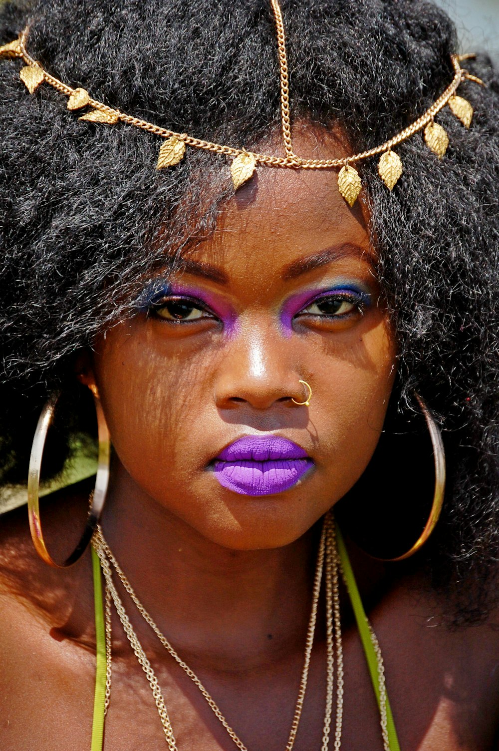 woman with black hair wears gold-colored nose ring, pair of loop earrings and purple lipstick