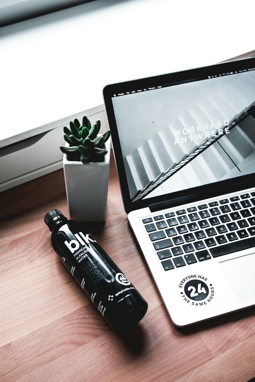 Blk. plastic bottle near MacBook Pro and potted green succulent plant all on brown woode ntable