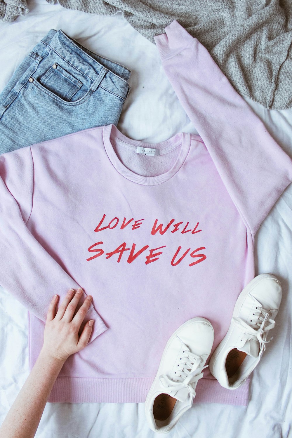 pink long-sleeved shirt on white textile near white low-top sneakers and blue denim bottoms