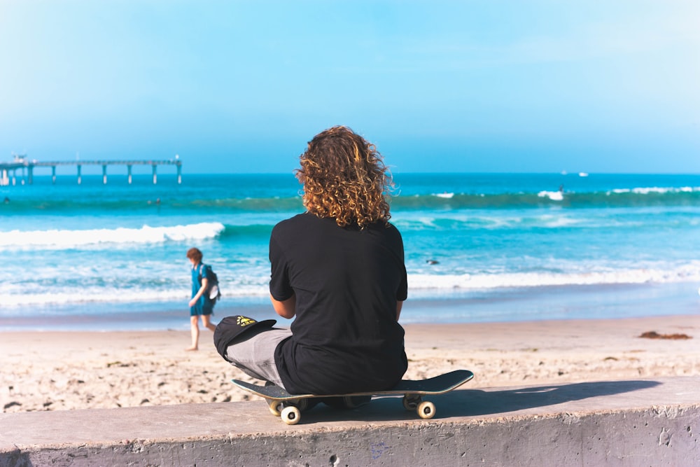 person sitting on skateboard with sea shore background