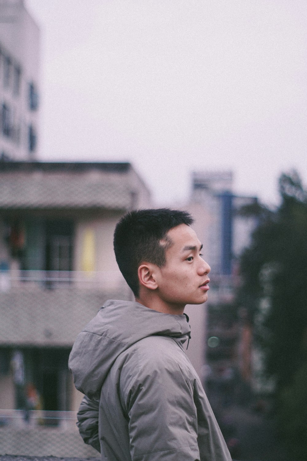 person standing in front of green tree and gray building