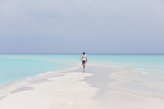 A serene beach with turquoise waters and a lone traveler walking along the shore.