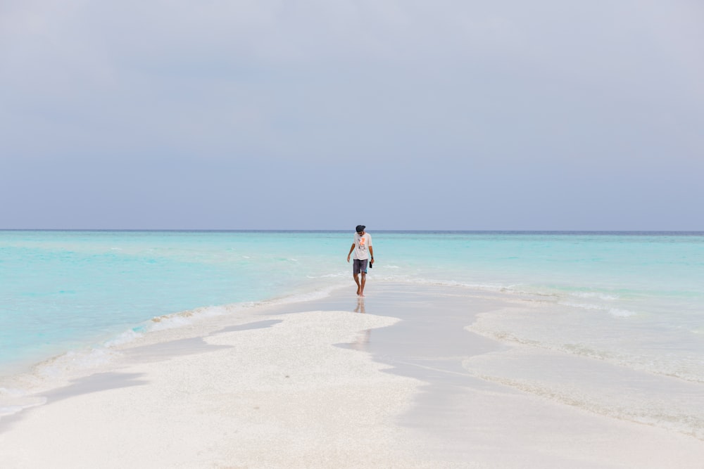 person wearing white shirt walking on seashore near blue body of water under blue sky during daytime