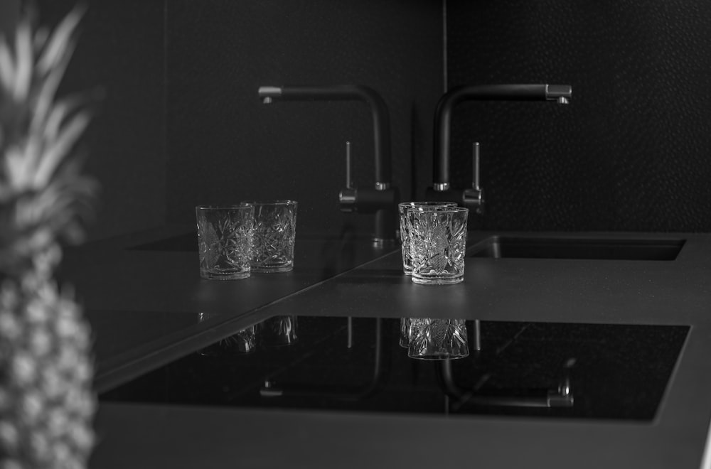 grayscale photo of two rocks glass near sink