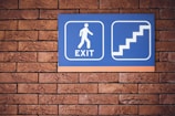 blue and white exit signage mounted on brown brick wall