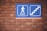 A blue sign with a white figure walking towards the word 'EXIT' accompanied by a graphic of stairs is mounted on a brick wall.