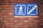 A blue sign with a white figure walking towards the word 'EXIT' accompanied by a graphic of stairs is mounted on a brick wall.