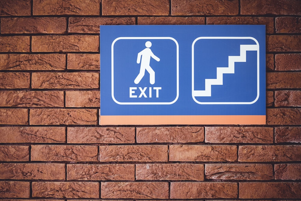 blue and white exit signage mounted on brown brick wall