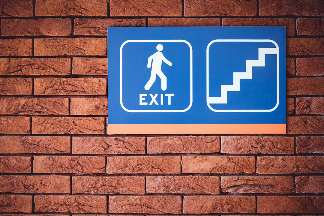 blue and white exit signage mounted on brown brick wall