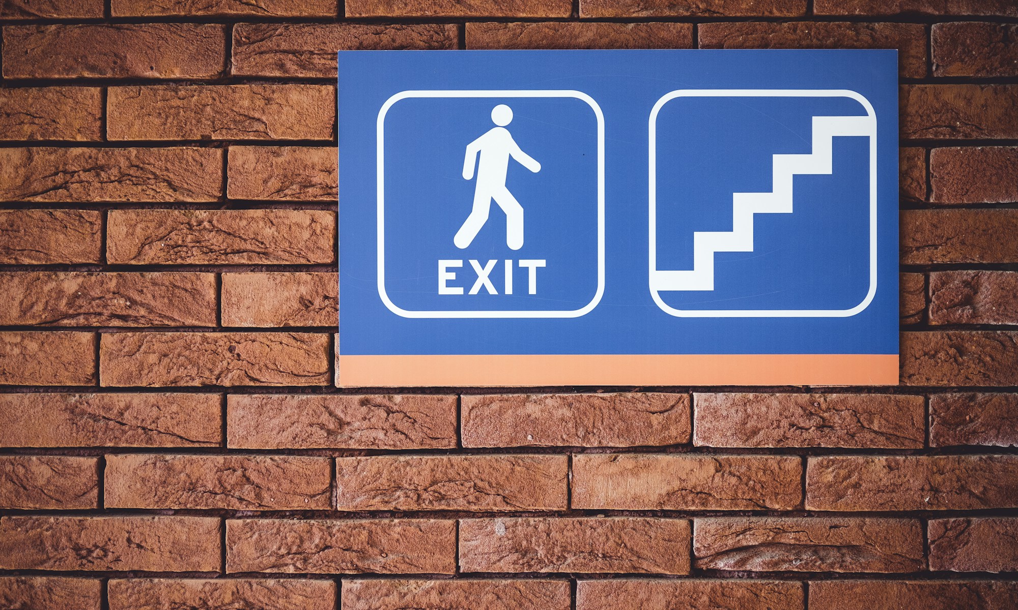 blue and white exit signage mounted on brown brick wall