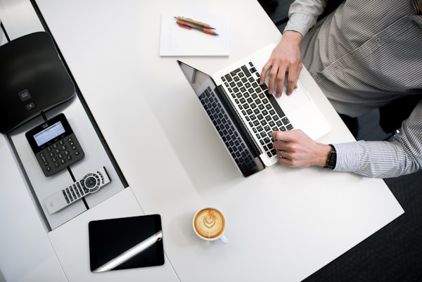 personne portant une chemise à rayures et travaillant sur un ordinateur portable avec un café et une tablette tactile