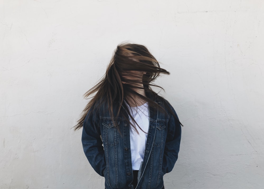 woman wearing blue denim jacket standing near white concrete wall