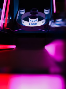 An arcade skee-ball machine with glowing neon lights surrounding the playfield. The machine's rings are labeled with numbers like 1,000, 2,000, and 10,000, indicating point values. The photo captures a vibrant and futuristic feel with an emphasis on the fluorescent glow.