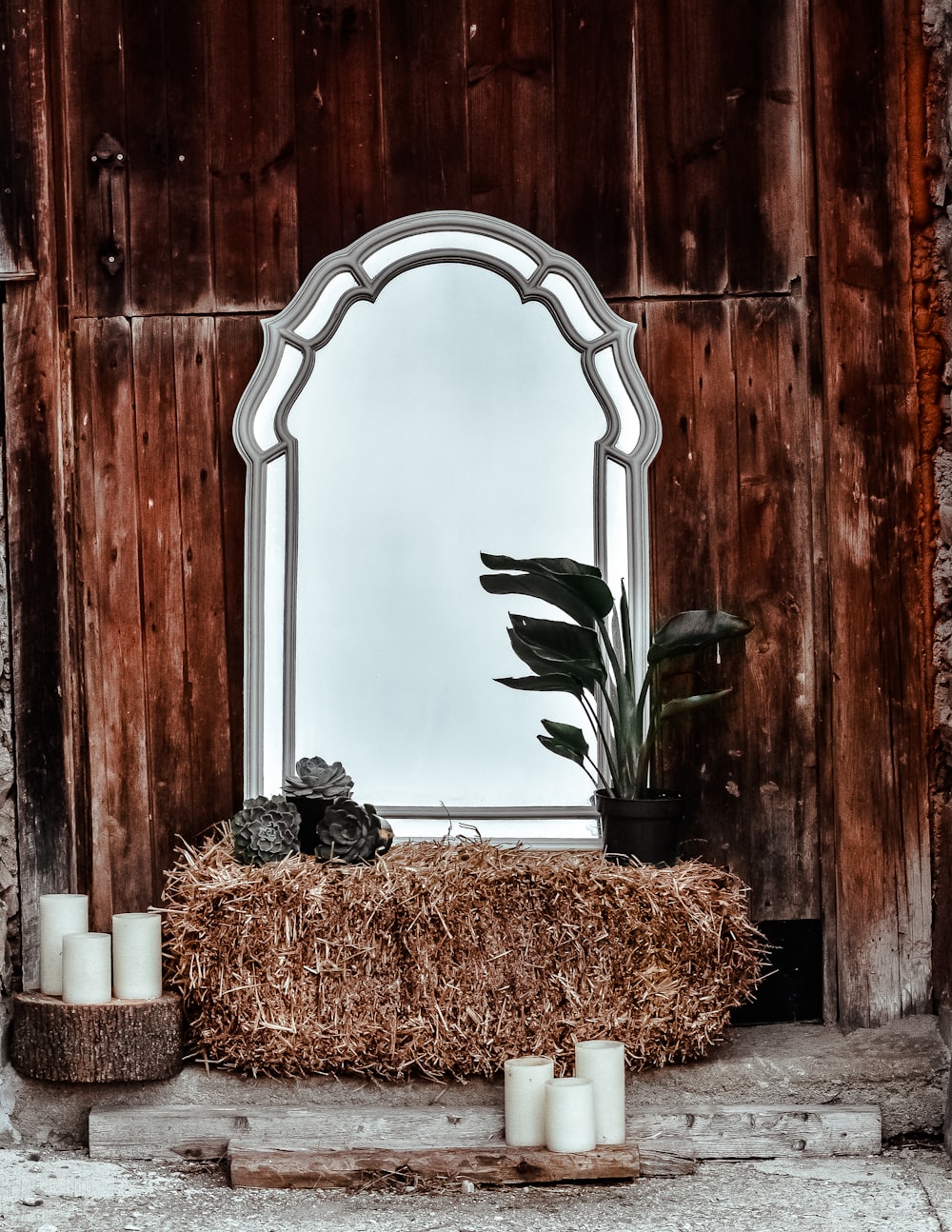 회색 프레임 기울어 거울 건초와 화분에 심은 녹색 잎 식물