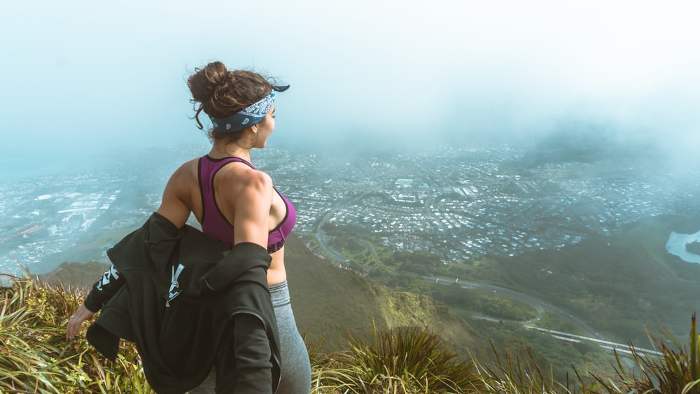 Mujer en sujetador deportivo rosa y polainas grises con vistas al horizonte de la ciudad desde una montaña con niebla durante el día