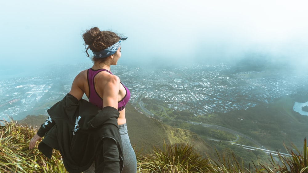 woman in pink sports bra and grey leggings overlooking city skyline from a mountain with fogs during daytime