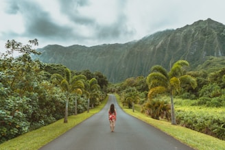 woman walking in black concrete road in front of mountain