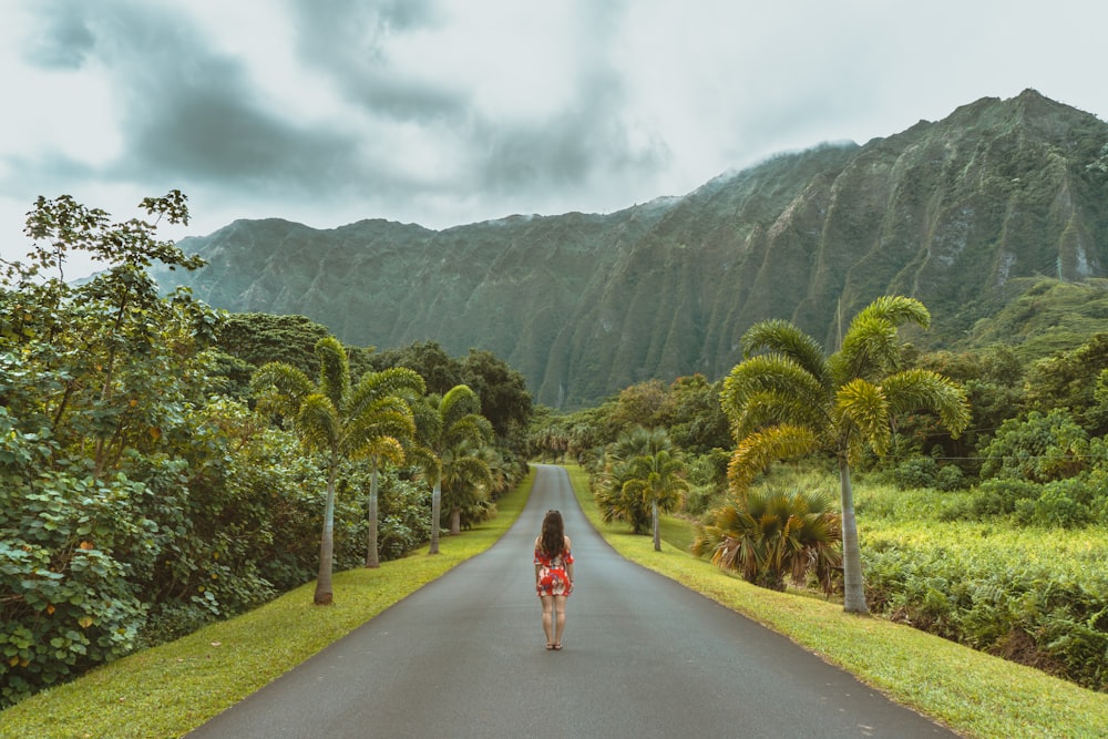 woman walking in black concrete road in front of mountain