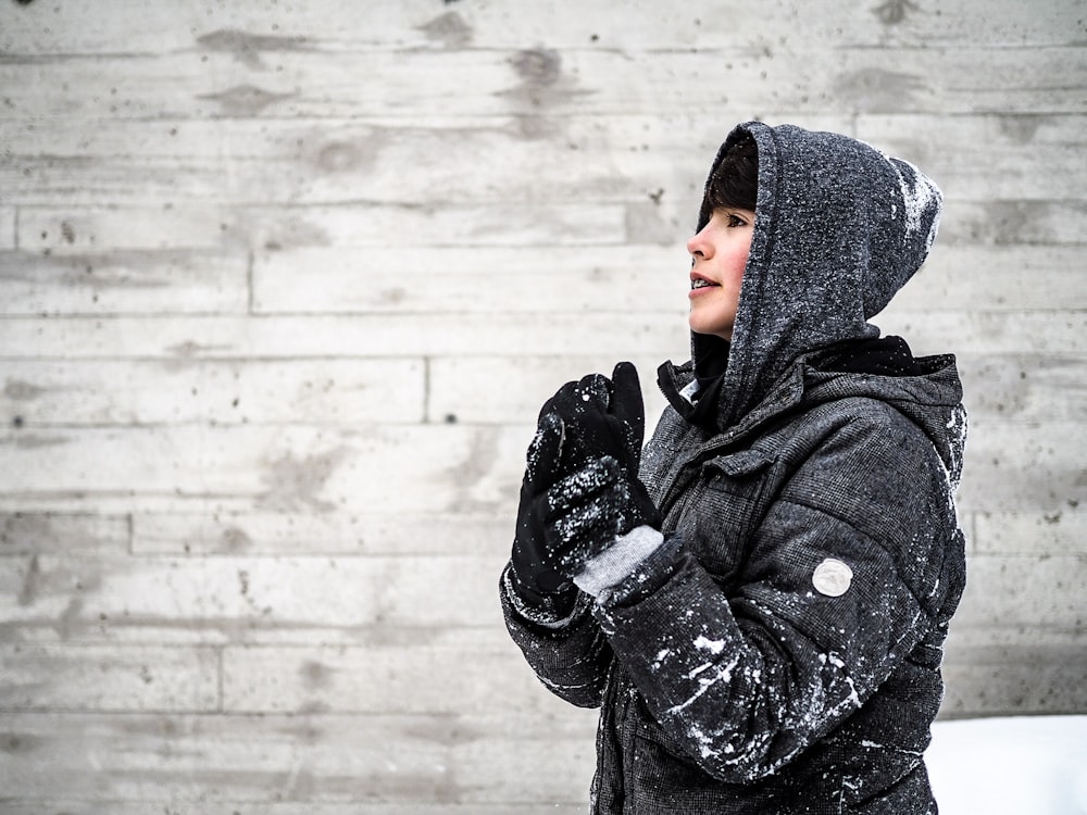 person wearing black hooded jacket standing beside grey wall