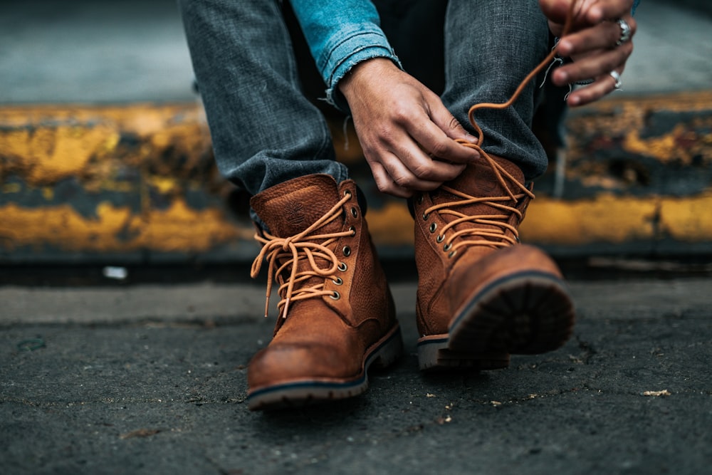 person sitting on yellow gutter tying up his left boot's laces