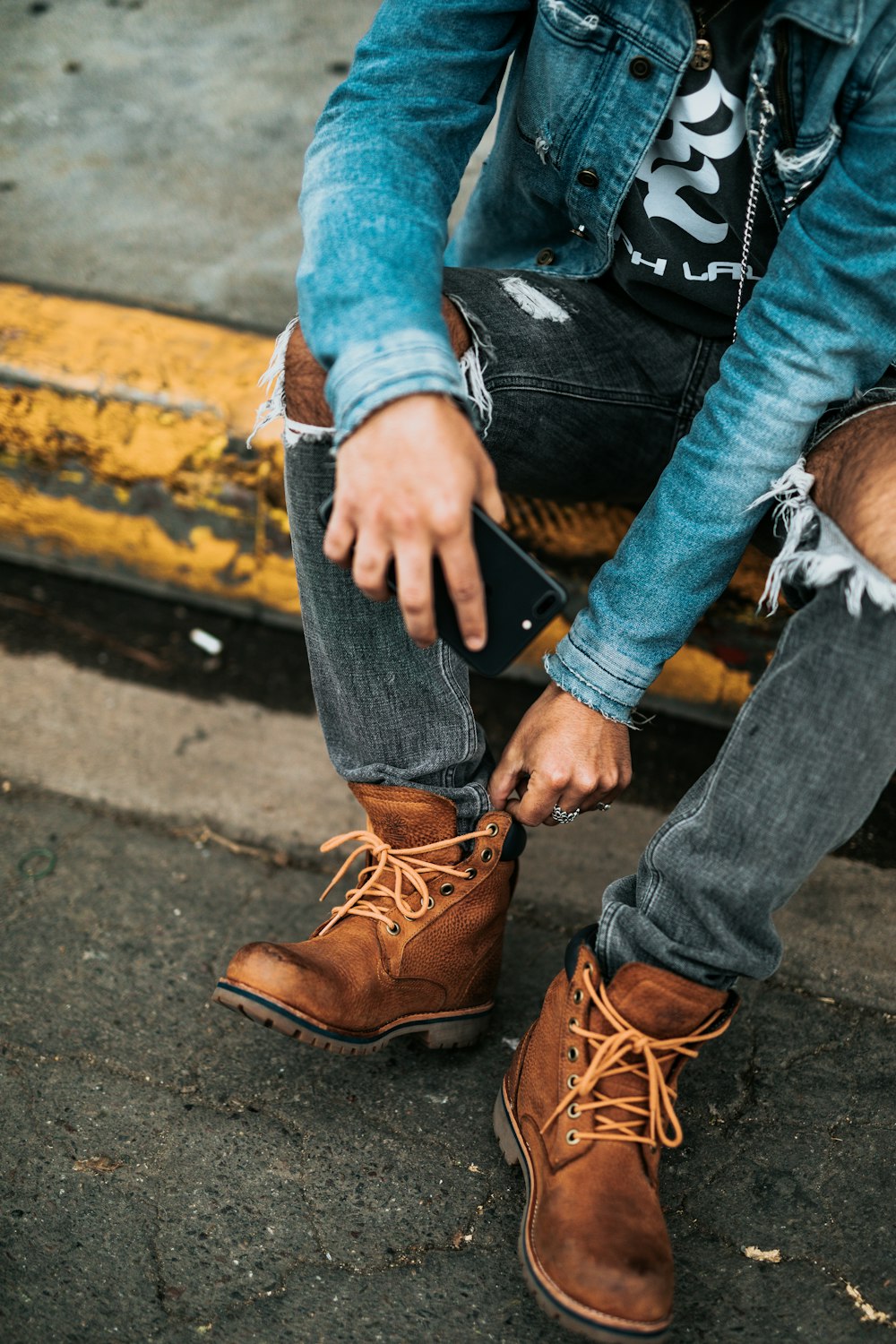 personne portant une paire de bottes brunes, un jean ajusté usé et une veste en jean