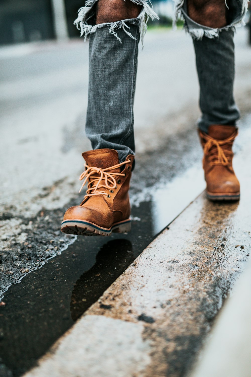 Persona in jeans grigi e stivali di pelle marrone che cammina sulla strada