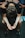 A person is sitting with their head bent forward, arms resting on their knees, and palms open in a pleading or contemplative gesture. Multiple hands are laid on their back, suggesting support or comfort from others around them. The atmosphere feels solemn and empathetic.