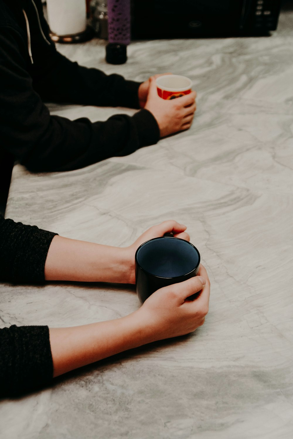 two person holding black and red ceramic mugs