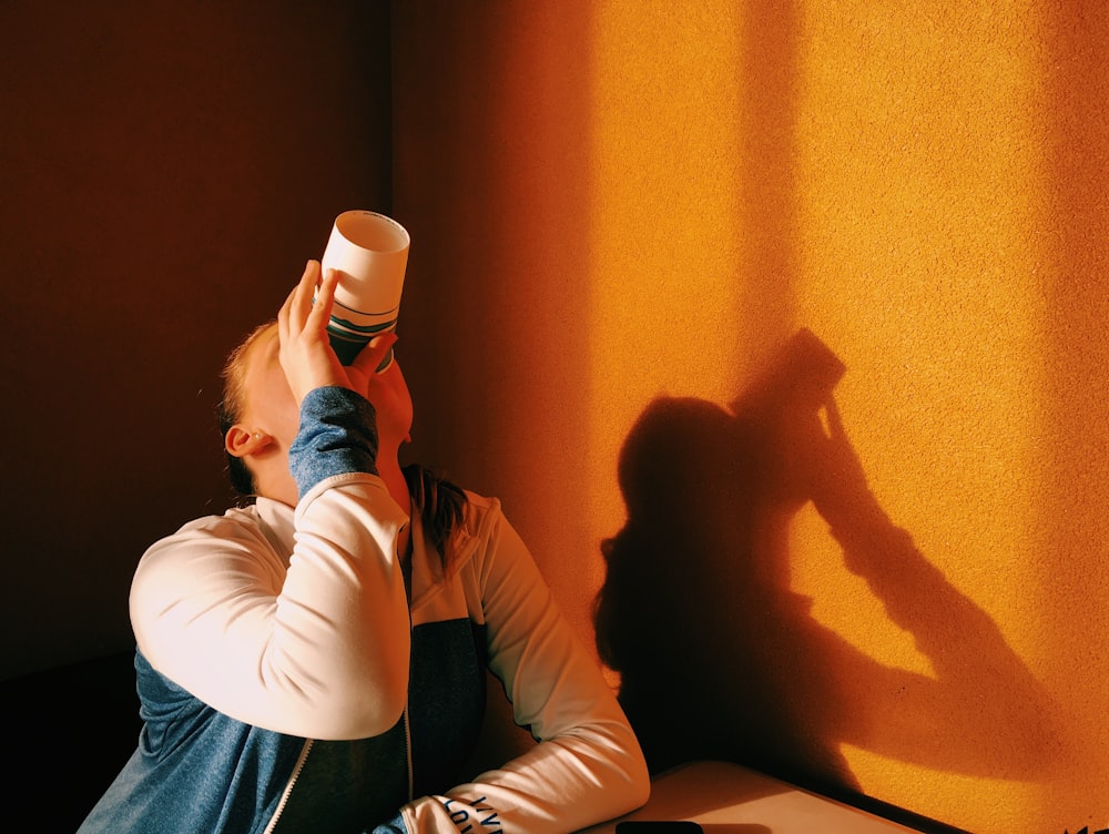 person in white and blue jacket drinking during orange sunset