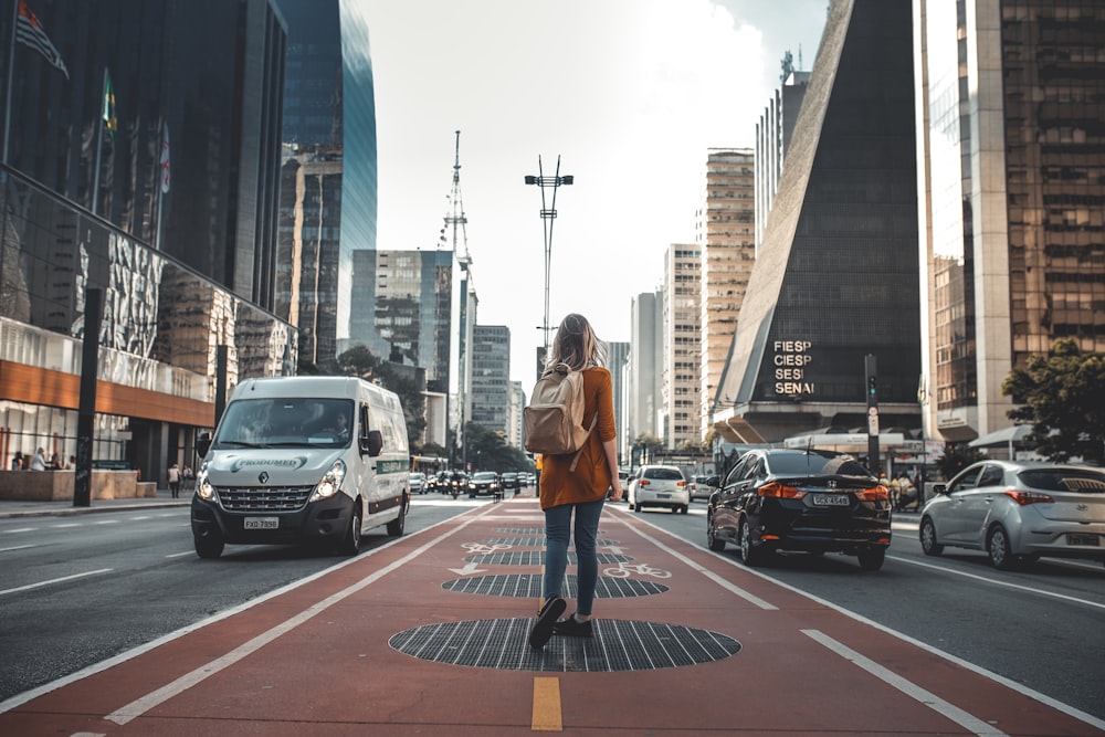 photography of woman walking in between road with vehicles