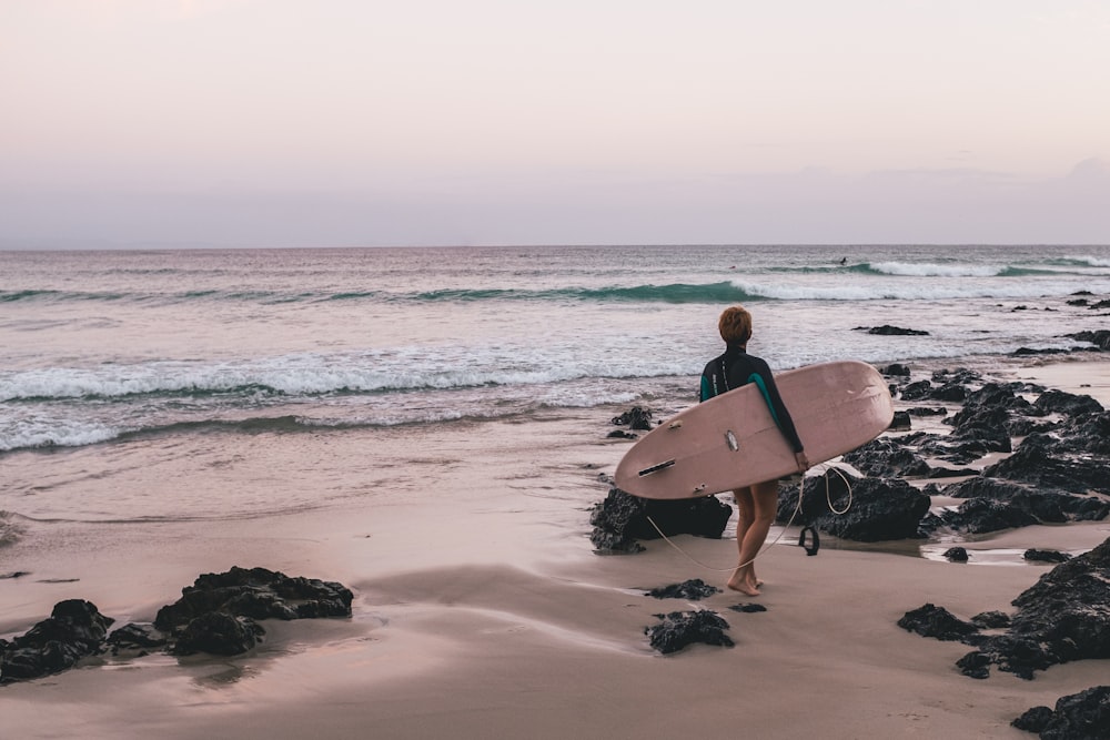 Mujer que lleva una tabla de surf en la orilla del mar
