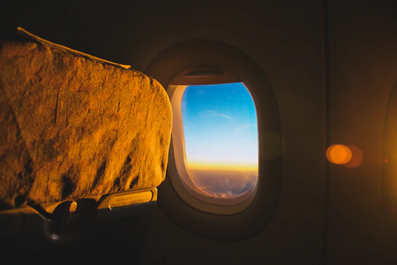 A cozy airplane window seat bathed in warm sunset light, with a travel journal and a cup of chai on the tray table.