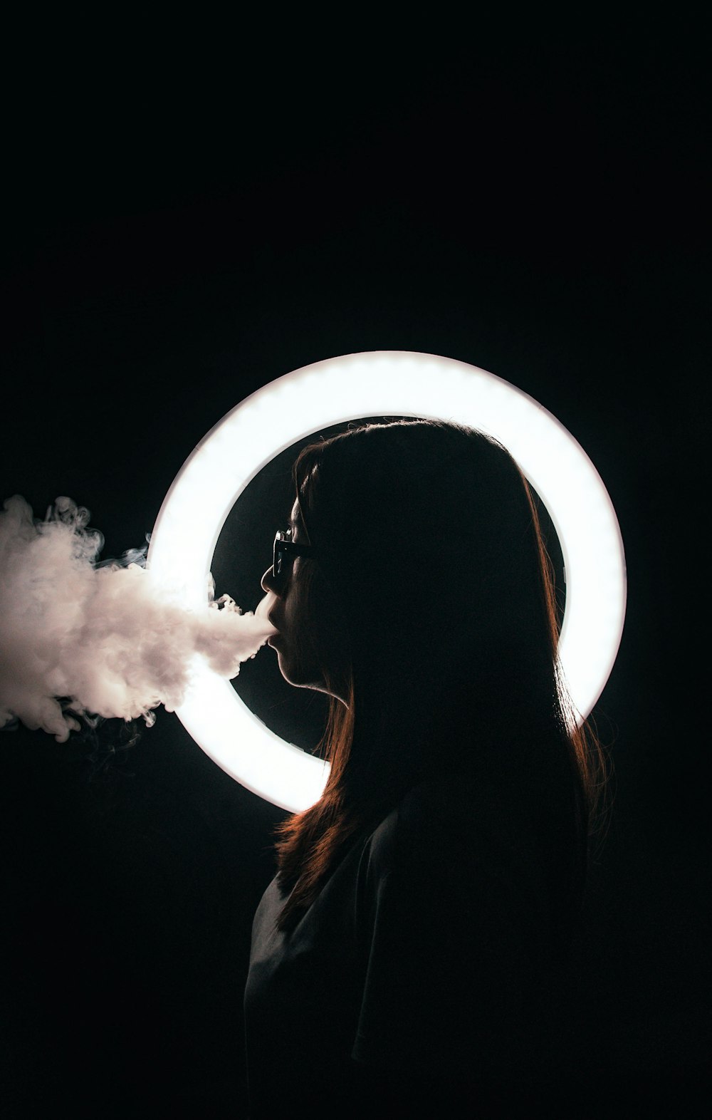 丸い電球のそばに立って煙草を吸う女性