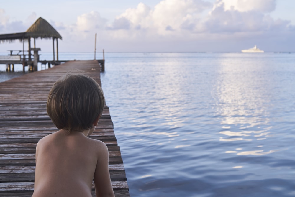 Niño arrodillado en el muelle de madera