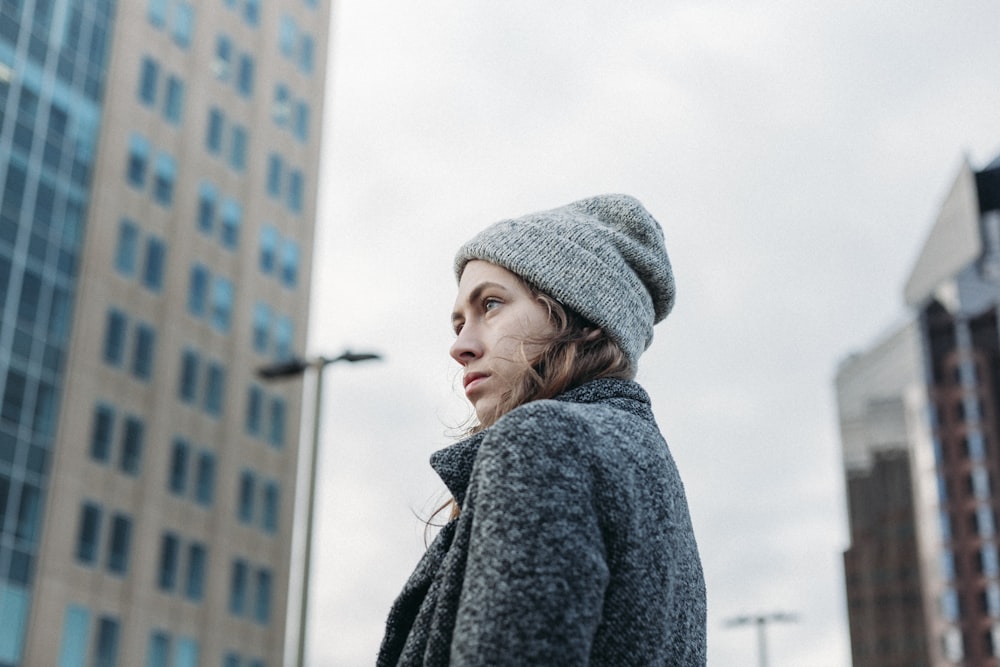 woman wearing gray coat knit cap standing near building during daytime