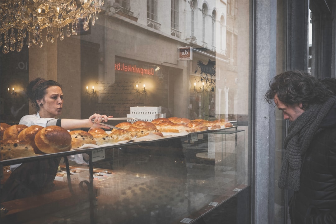 man facing storefront in front of woman holding thong picking bread