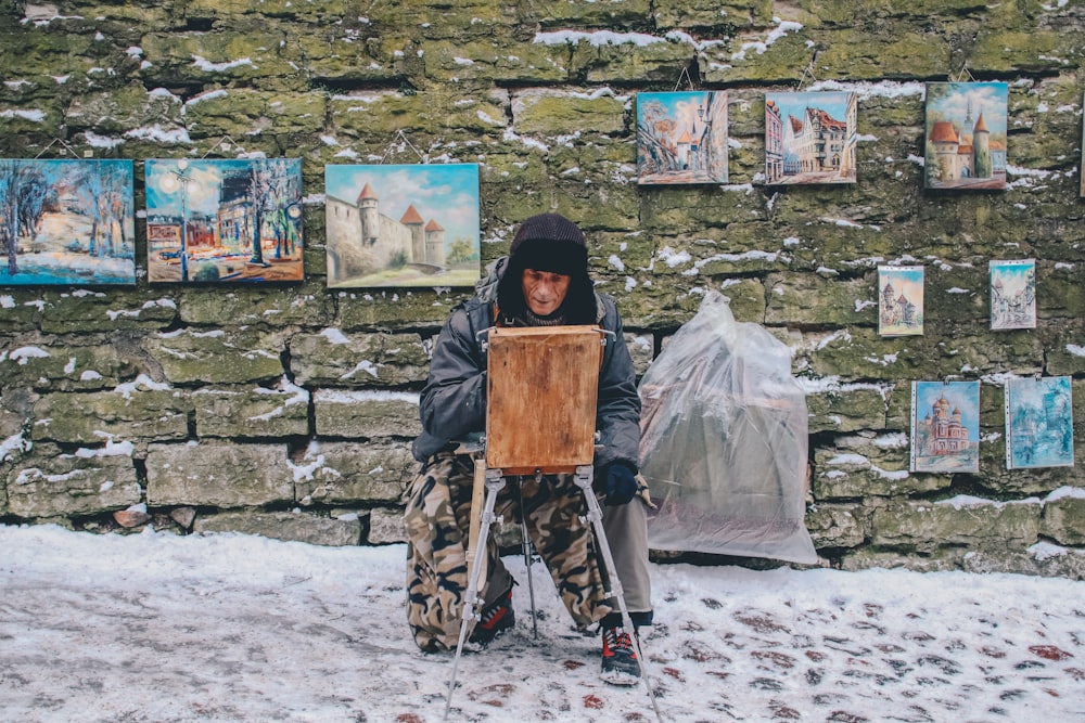 homem pintando na frente da parede com suas obras penduradas